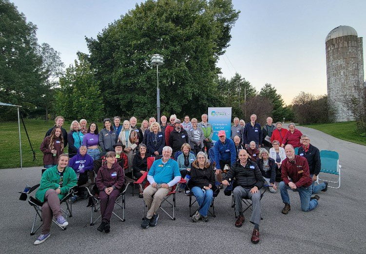 Group photo of about 50 adults from the conservation social event in Appleton, outdoors on paved area near trees and a silo